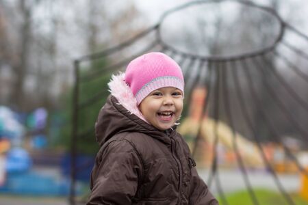 Laughing little girl looking at camera and waving in autumn parkの写真素材