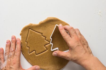 Woman hands cutting forms of christmas tree on rolled out gingerbread dough on the white backgroundの写真素材
