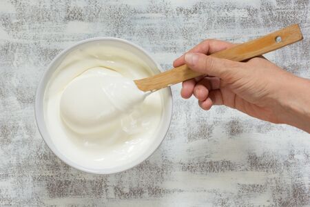 Sour cream in white bowl with wooden spoon in woman hand on the white backgroundの写真素材