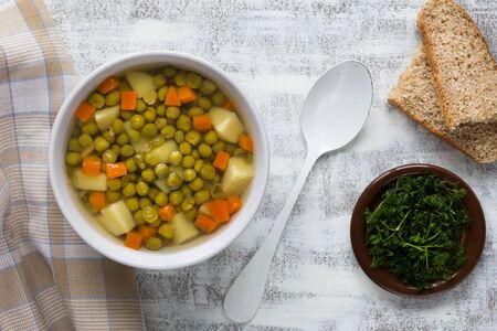 Soup with green peas and vegetables in white bowl on the white backgroundの写真素材