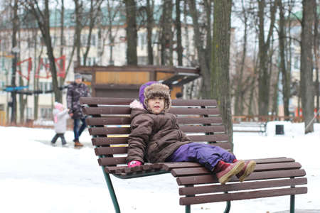 Side view of caucasian child sitting on bench in winter parkの写真素材