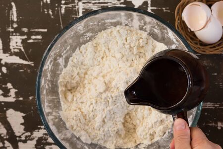 Woman hand holding ladle with hot water to put it into flour to make dough on brown background