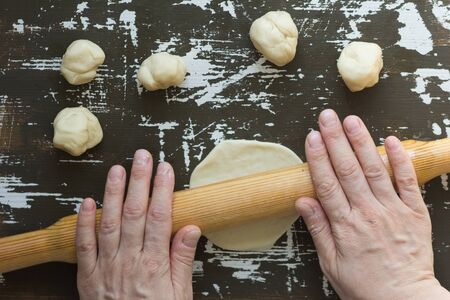 Small balls of dough rolled by woman hands for making vareniki on brown background