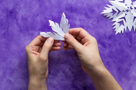 Woman hands unfolding paper to reveal snowflake on violet surfaceの写真素材