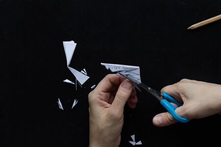 Making snowflake. Step 12. Woman hands cutting away shapes from the edges of the paper to shape snowflake pattern on black backgroundの写真素材