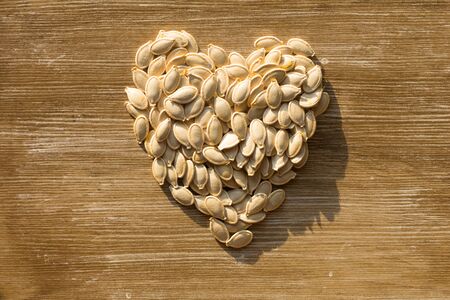 Top view of raw seeds pumpkin in shape of heart on wooden background. Concept healthy for heart.の写真素材