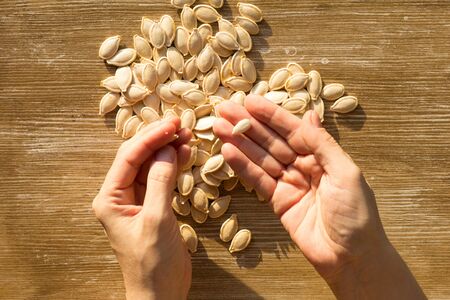Top view of raw seeds pumpkin and one peeled off seed on woman hand on wooden backgroundの写真素材
