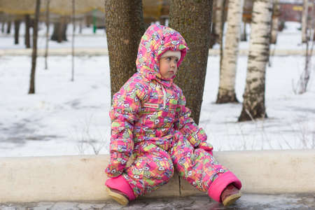 Cheboksary Russia - 9 January 2020: Child in winter cloth sitting on panel on ground in winter park and looking asideのeditorial素材