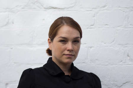 Portrait of serious caucasian middle aged woman looking at camera with soft look on white brick...