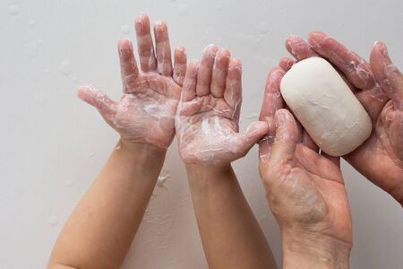 Top view of soaped child and woman hands holding soap on white background