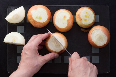 Top view of woman hands cutting in half unpeeled onion on black backgroundの写真素材