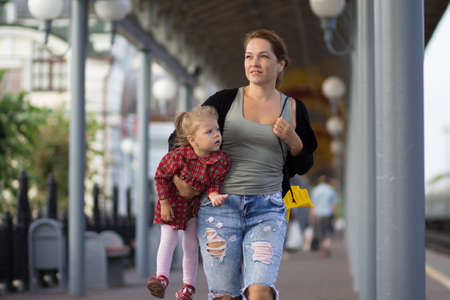 Mother holding and carrying caucasian child of two years old on paving stones and looking aside in summertimeの写真素材