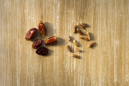 Top view of heap of date fruit and bones as seeds for planting palm on wooden background