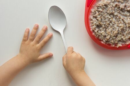 Top view of child hands holding spoon in right hand and buckwheat porridge on white backgroundの写真素材