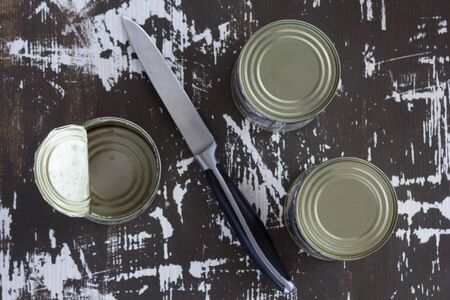 Top view of two closed cans and one open can with knife on the wooden backgroundの写真素材