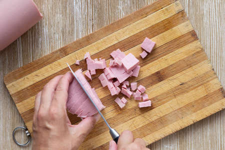 Top view of woman hands cutting sausage on wooden cutting board using knife