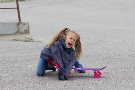 Crying caucasian girl of five years falling from skateboard in summer parkの写真素材