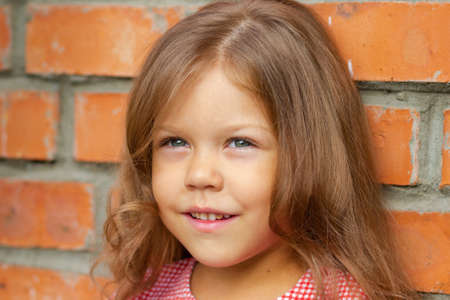 Smiling caucasian little girl of five years old looking aside on brick backgroundの写真素材