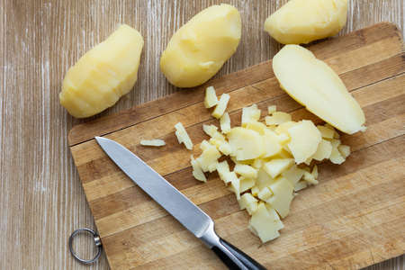 Top view of cutted scrubbed boiled potatoes in jackets using knife on wooden backgroundの写真素材