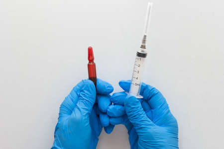 Top view of woman hands in medical gloves holding two ml ampoule with vitamin group B for injection and five ml syringe barrelの写真素材