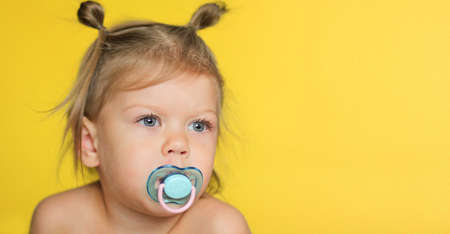 Portrait of cute caucasian child kid little girl of 2 years with pacifier in mouth on the yellow background with copy spaceの写真素材