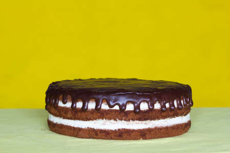 Chocolate cake with white cream and chocolate drops on the yellow background