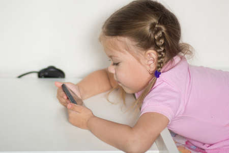 Caucasian child of three age holding mobile phone and looking at it on the white background