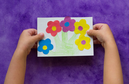 Handmade greeting card with flowers in child hands on the purple background