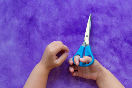 Scissors in child hands on the purple backgroundの写真素材