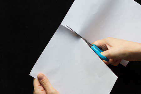 Woman hands cutting rectangular sheet of paper in half on black backgroundの写真素材