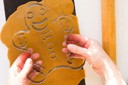 Woman hands holding metal form of gingerbread man before cutting it out on raw dough black baking sheet on white backgroundの写真素材