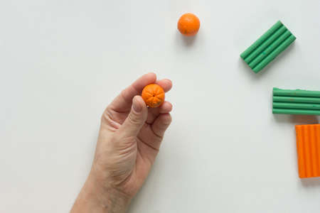 Woman hands showing dot on orange ball to create orange fruit from the polymer clay