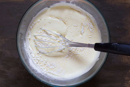 Top view of glass bowl with whiskey, dry ingredients and batter on the wooden background