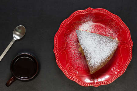Top view of piece of apple cake on red plate on the black background