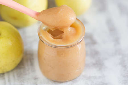 Apple sauce in glass jar and spoon on the white background