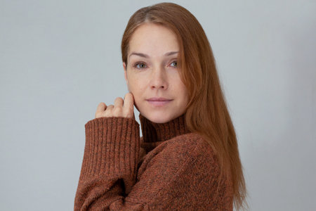 Portrait of middle aged woman with reddish hair in reddish brown sweater looking at camera holding...