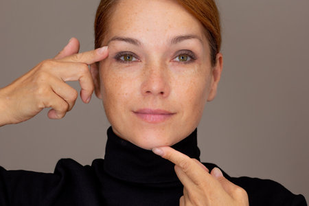 Portrait of woman with freckles showing on eyelid and chin by fingersの写真素材