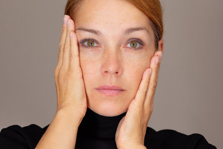 Portrait woman looking at camera holding palms on cheeks surprised of soft skinの写真素材
