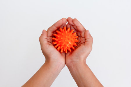Child hands holding orange spiky ball for massage over white background