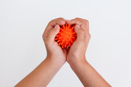 Child hands holding orange spiky ball for massage over white backgroundの写真素材