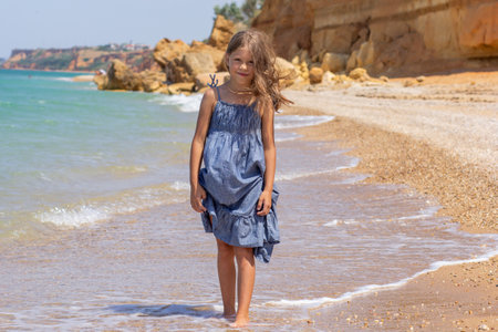 Person in a blue dress standing on a beach shore on a sunny summer dayの写真素材