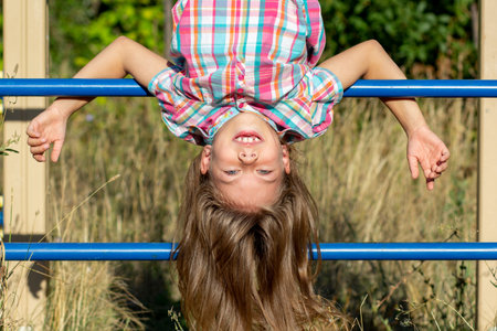 Portrait of smiling caucasian child 7 8 years hanging upside down on wall bars outside