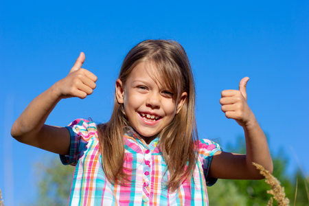 Portrait of smiling caucasian child 7 8 years showing thumb up on blue skyの写真素材
