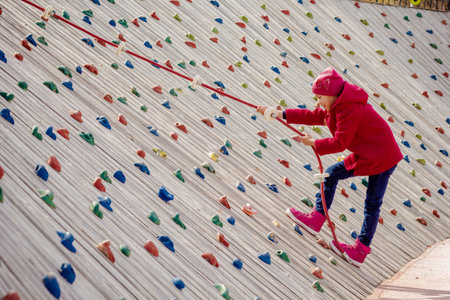 Happy child climbing on artificial rock wall using rope on playgroundの写真素材