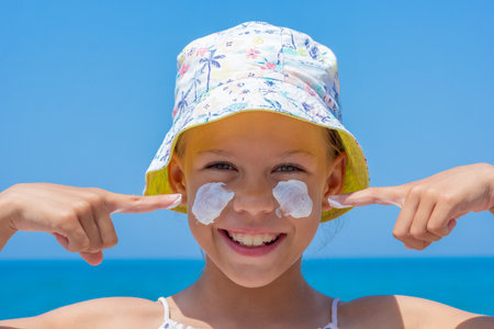 Caucasian smiling child of 8 9 years in a sun hat showing on sunscreen on cheeks over sea looking at...