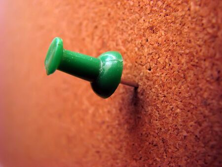 Green plastic pushpin on brown corkwood board.の写真素材