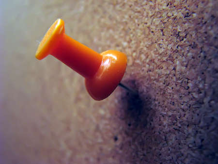 Orange plastic pushpin on brown corkwood board.の写真素材