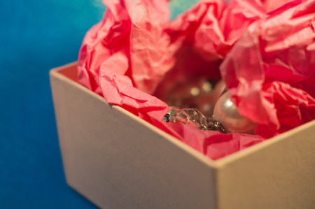 Light-coloured opened square present box without lid with pink paper and jewellery inside on the blue backgroundの写真素材