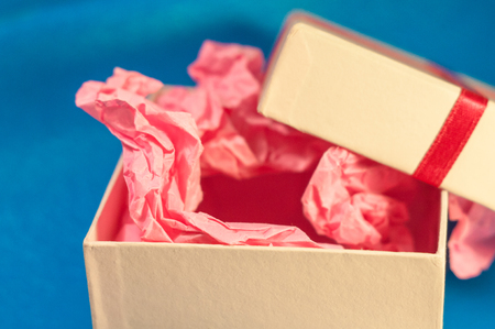 Light-coloured opened square present box without lid with pink paper inside on the blue background
