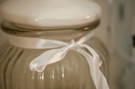 A glass can with decorative white ribbon and a bowの写真素材
